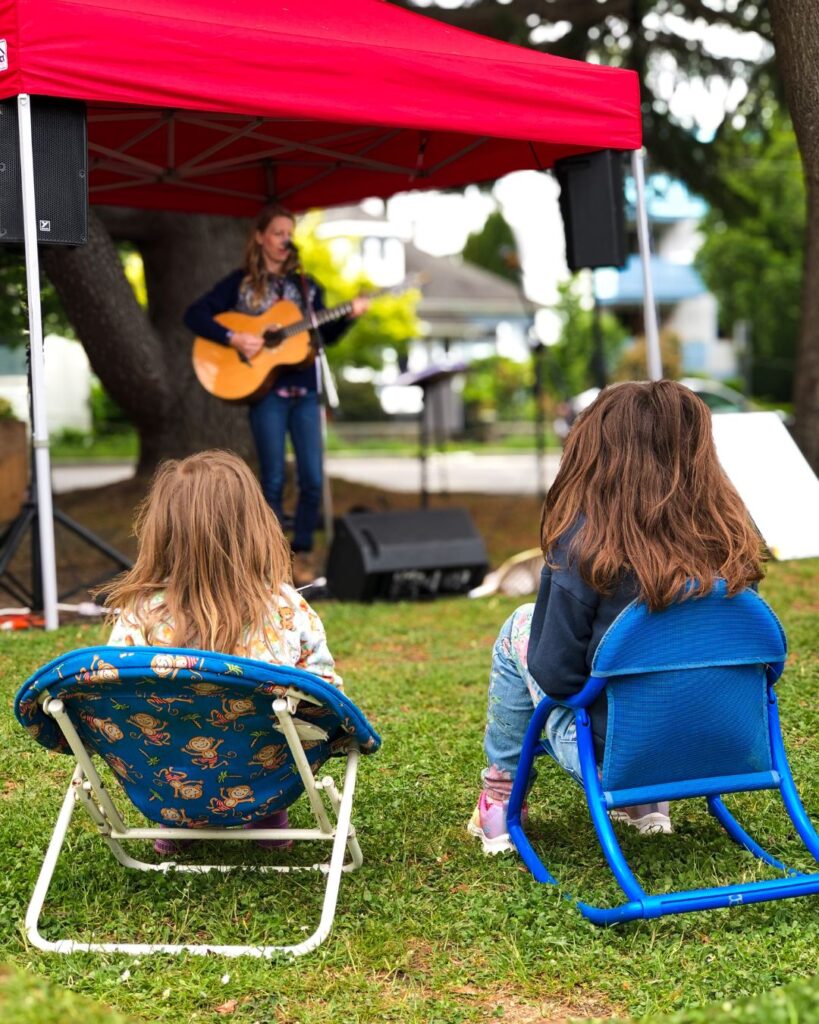 James Bay Market Music Post - photo is Carla Olive playing and two young fans sitting in their lawn-chairs listening.