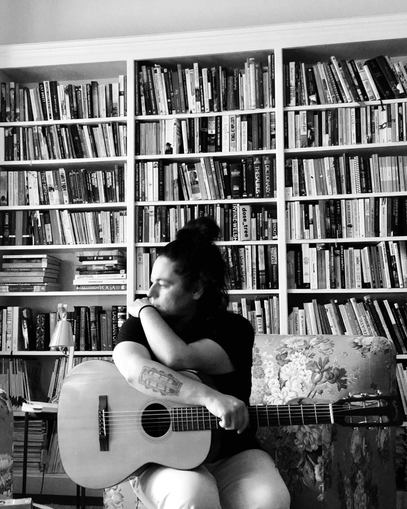 james bay market 2025 June Music line-up: photo of Marina Avros with her guitar in front of a large bookshelf.