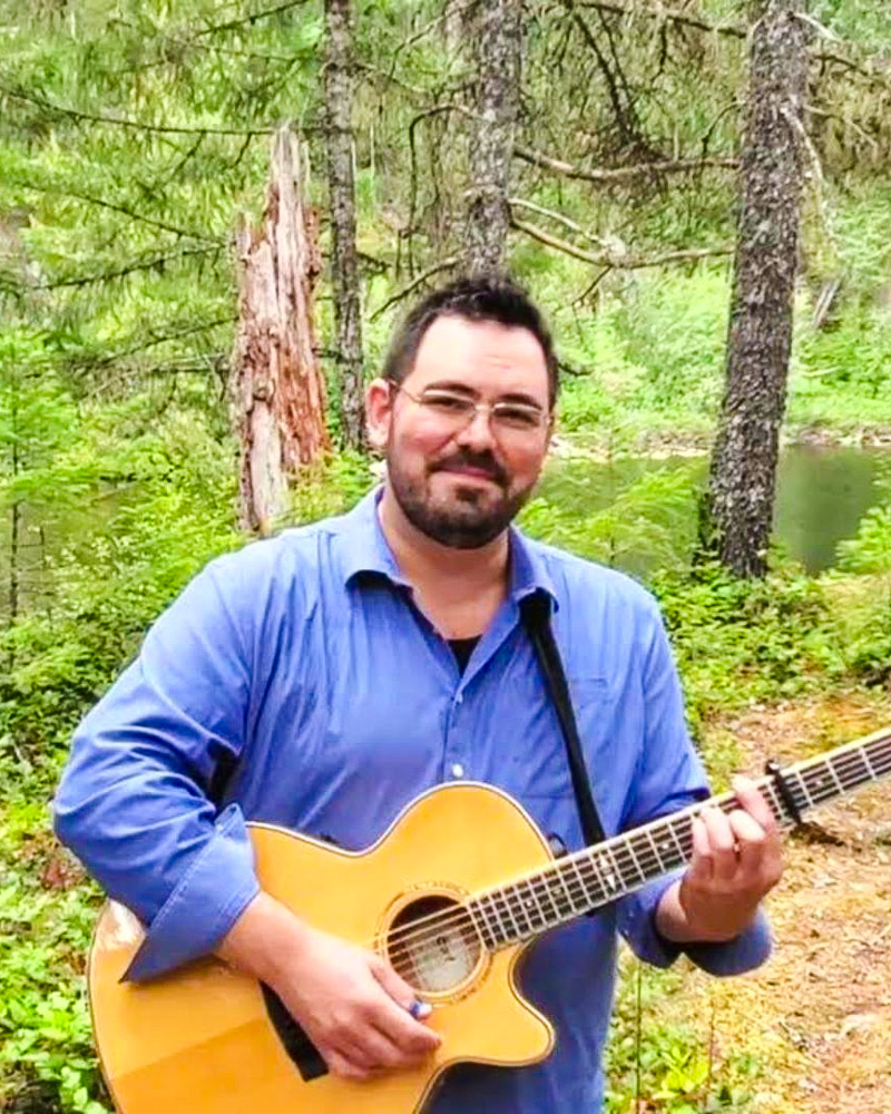 James Bay Market - 2025 June Music Line-up. Photo has Rob Fillo standing in the woods holding his guitar.
